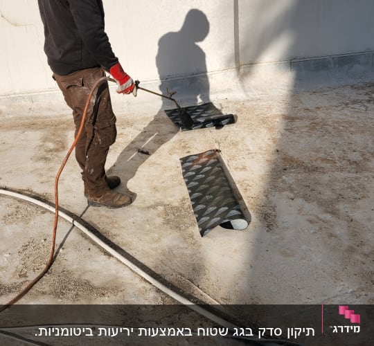 אדם עם מבער מחמם יריעות איטום על גג